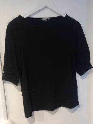 Svart topp med puffärm från H&M - Snygg svart topp från H&M med puffiga halvlånga ärmar och rak passform. Enkel och stilren design som passar till det mesta. Tillverkad i mjukt tyg för en bekväm känsla.
