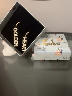 Ioaku örhängen med text och strass - Statementörhängen från Ioaku i guldtonad metall med gnistrande strass. Ena örhänget har texten 'GOLDEN' och det andra 'HEART' i stora bokstäver. Perfekta för dig som vill sticka ut och addera lite extra bling till din stil. Använda en gång. Skicka gärna prisförslag eller frågor 
