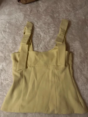 Gul linnetopp med breda axelband - Söt gul linnetopp med breda axelband. Toppen har en rak skärning och är ärmlös, perfekt för varma dagar. Materialet känns mjukt och lätt, vilket gör den superbekväm att bära. Enkel men ändå stylish design som passar till mycket. Slutsåld överallt
