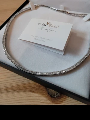 Vidal & Vidal halsband i silver - Snyggt halsband från Vidal & Vidal i 925 silver med platina-plätering. Halsbandet har en elegant, fyrkantig design med gnistrande stenar längs hela kedjan. Perfekt för dig som gillar stilrena och exklusiva accessoarer.