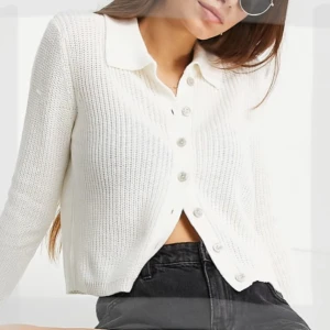 Vit stickad crop kofta från Stradivarius - Snygg vit stickad kofta från Stradivarius med krage och knappar framtill. Modellen är croppad och har långa ärmar. Perfekt att slänga över ett linne eller t-shirt för en chill look.