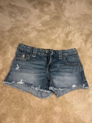 Blå jeansshorts med fransig kant - Ett par blå jeansshorts med fransig kant och lite slitna detaljer, andvända 5-10 gånger (pris kan diskuteras)
