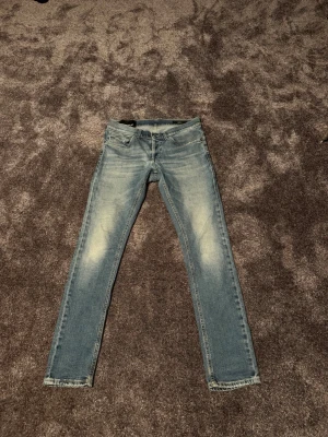 Ljusblå Dondup jeans George - Säljer ett par ljusblå Dondup jeans med snygga slitningar och klassisk femficksdesign. Jeansen har en smal passform och är perfekta för en avslappnad och trendig look. Fint detaljerade sömmar och dragkedja vid gylfen. Finns en defekt vid skrevet som ej märks vid användning därav priset!