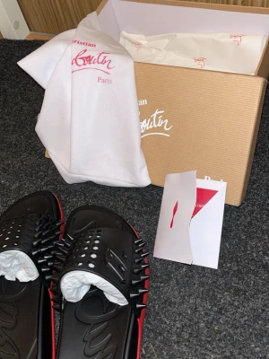 Svarta spikprydda sandaler Louboutin - Coola svarta sandaler från Christian Louboutin med ikoniska röda sulor och silverfärgade nitar över remmen. Tillverkade i gummi med en chunky design och tydlig logga på sulan. Perfekta för dig som vill sticka ut med edgy detaljer.
