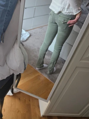  True religon Ljusgröna jeans med fickdetaljer - Snygga ljusgröna jeans med låg midja och dekorativa fickor bak med lock och knapp. Jeansen har klassisk femficksdesign och smal passform som sitter tajt längs benen. Perfekta för dig som vill ha en fräsch och trendig look.