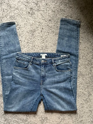 Blå skinny jeans med hög midja - Säljer ett par klassiska blå skinny jeans med hög midja och fem fickor. Jeansen har en snygg tvättad look och smal passform hela vägen ner. Perfekta till vardags och lätta att matcha med olika stilar. Materialet är denim i bomull med lite stretch.