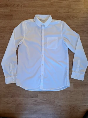 Vit skjorta från H&M med bröstficka - Ny/oanvänd vit skjorta från H&M med lång ärm och bröstficka. Skjortan har knappar framtill och vid ärmsluten samt en stilren krage. Perfekt för festen, högtiden eller dig som gillar klassisk stil. Easy iron. Obs! Tags saknas. 