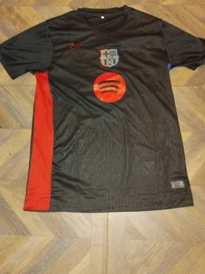 Svart FC Barcelona matchtröja Nike - Säljer en svart FC Barcelona matchtröja från Nike med klubbmärke och röd Spotify-logga på bröstet. Tröjan har röda och blå detaljer på sidorna och är tillverkad i ett lätt, ventilerande material som passar perfekt till träning eller match.