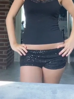 Svarta paljettshorts med låg midja - Säljer ett par svarta shorts med paljetter som ger en glittrig look. Shortsen har låg midja och en tight passform, perfekta för dig som vill sticka ut lite extra. Passar till sommarens alla äventyr!