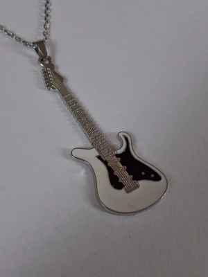 Halsband med elgitarr-hänge - Snyggt halsband med ett hänge i en elgitarr. Hänget är i silverfärgad metall med vita och svarta detaljer som liknar en klassisk elgitarr. Materialet rostfritt stål. 