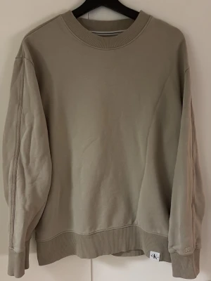 Calvin Klein sweatshirt - Snygg beige sweatshirt från Calvin Klein Jeans med rund halsringning och ribbade muddar vid ärmslut och nederkant. Tröjan har en relaxed fit och en liten CK-logga på nederkanten. Perfekt för en avslappnad och stilren look.