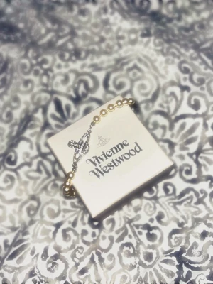 Vivienne Westwood armband - Säljer ett snyggt armband från Vivienne Westwood med vita pärlor och ett ikoniskt silverfärgat orb-hänge med gnistrande stenar. Perfekt accessoar för dig som gillar statement-smycken och vill ha något som sticker ut.(kan diskutera priset)😊