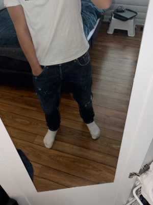 Mörkblå slim fit jeans med slitningar - Säljer ett par mörkblå slim fit jeans med snygga slitningar och detaljer på benen. Jeansen har klassisk femficksdesign och sitter tajt vid anklarna. Perfekta för dig som gillar en trendig och avslappnad stil.