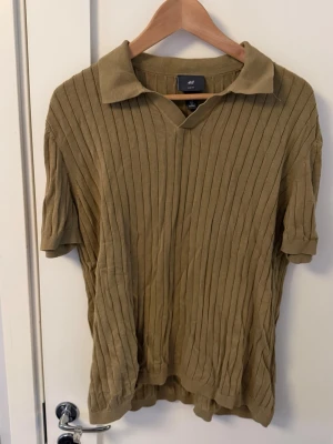 Ribbad beige polotopp med krage - Säljer en ribbad beige polotopp från H&M med korta ärmar och klassisk krage. Modellen är i slim fit.