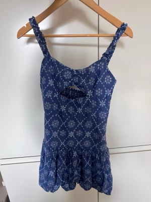 Blå populär klänning från Zara - Söt blå klänning från Zara med vita broderade blommor och smockade axelband. Klänningen har en liten cut-out framtill och volang nedtill. Perfekt för varma dagar och ger en avslappnad men trendig look.