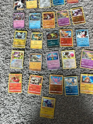 Samling Pokémonkort blandade typer - Säljer en samling med 28 Pokémonkort i olika färger och typer. Korten har klassisk blå baksida och motiv på olika Pokémon på framsidan. Perfekt för dig som vill utöka din samling eller börja spela Pokémon TCG. Blandade motiv och energityper.