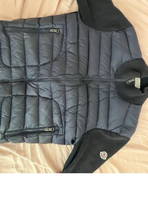 Moncler Cardigan  - Snygg pufferjacka från Moncler med quiltad framsida och två dragkedjeförsedda fickor. Ärmar och rygg i mjukt tyg, ribbad krage och Moncler-logga på ena ärmen. Storlek M 2 men passar även S