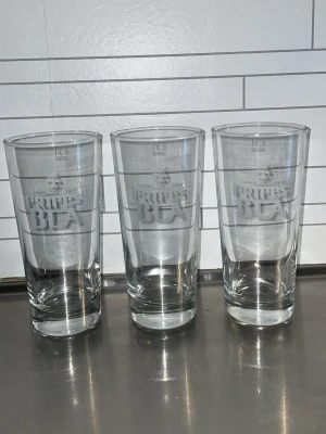 Tre Pripps Blå ölglas 80kr st - Säljer tre höga ölglas från Pripps Blå med logga ingraverad på framsidan. Glasen är genomskinliga och rymmer 50 cl. Perfekta till hemmabaren eller för att servera kall öl med stil.