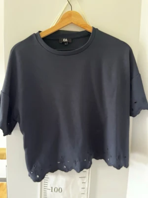Mörkblå t-shirt från C&A - En mörkblå t-shirt från C&A med avslappnad passform och korta ärmar. T-shirten har rå kant nertill med små håldetaljer för en edgy look. Perfekt till jeans eller shorts för en chill stil. Den är croppad och jättefin, använd typ 1 gång