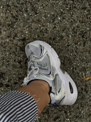 Vita och silver New Balance sneakers - Snygga 530 sneakers från New Balance i strl 36. Perfekta för en sportig och trendig look. Bra skick, använda fåtal gånger, säljer eftersom de är lite för små.