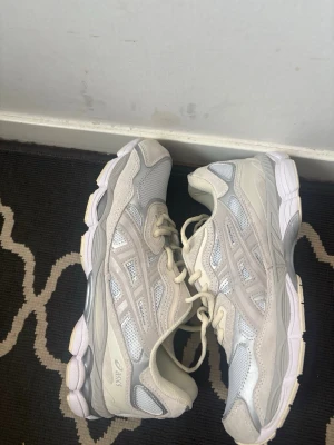 Vita och beige Asics sneakers - Snygga sneakers från Asics i vitt och beige med meshpaneler och detaljer i mocka. Perfekta för dig som gillar sportig och trendig stil.  Skorna är i mycket bra skick, skickar samma dag som köp