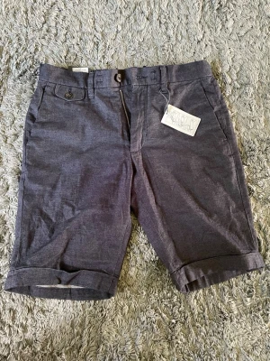 Mörkblå chinosshorts med knapp - Snygga mörkblå chinosshorts med knapp och dragkedja framtill. Klassisk passform med vikta benslut och sidofickor. Perfekta för varma dagar och stilrena outfits. Köptes för 600kr men säljs för halva priset, kan gå ner vid snabb affär.