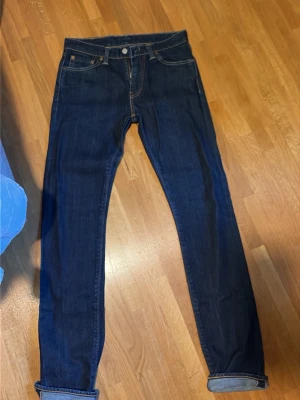 Levis selvedge jeans - Säljer ett par mörkblå selvedge jeans med raka ben och klassisk femficksdesign. Jeansen har uppvikta benslut och kontrastsömmar. Tillverkade i kraftigt denimtyg som ger en schysst och tidlös look. Har börjat få lite honeycombs o har potential för sjuka fades. 