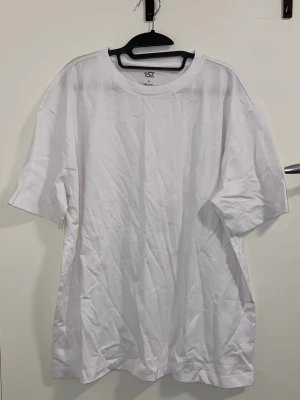 Vit basic t-shirt från 157 - Klassisk vit t-shirt från 157 i 100% bomull. Modellen har rund halsringning och korta ärmar, perfekt för en clean och enkel stil. Passar till allt och är ett måste i garderoben.  Storleken är M men den kan också vara som L eller XL 