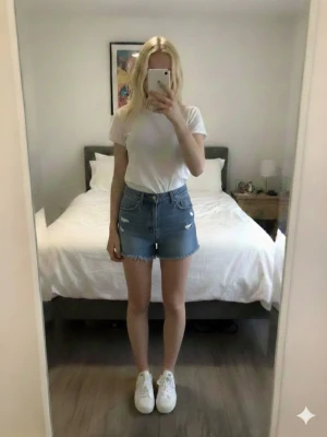 Blå jeansshorts med fransig kant - Säljer ett par klassiska blå jeansshorts med slitna detaljer och fransig kant nertill. Shortsen har fem fickor, bälteshällor och knappgylf. Perfekta för sommaren och ger en avslappnad vibe.