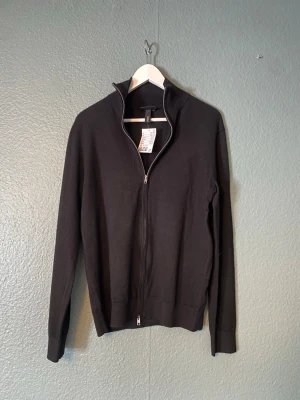 Svart ziptröja från H&M - Klassisk svart ziptröja från H&M med hög krage och hel dragkedja framtill. Tröjan har en enkel och stilren design, perfekt att bära över en t-shirt eller skjorta. Tillverkad i mjukt material för en bekväm känsla. Helt ny finstickad svart tröja storlek S från hm. Nypris 399 kr. 