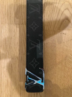 L\/ Bälte - Snyggt svart skärp från l med klassiskt monogrammönster och silverfärgat -spänne. Bältet är brett och har en lyxig känsla med detaljer i präglat skinn och kontrasterande sömmar på insidan.