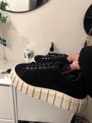 Svarta sneakers med chunky sula - Säljer ett par svarta eytys sneakers med grov, vit sula och svarta skosnören. Ovandelen är i mockaliknande material och sulan har en cool, räfflad design som sticker ut. Perfekta för dig som vill ha en unik look till vardagsoutfiten. Använda en gång