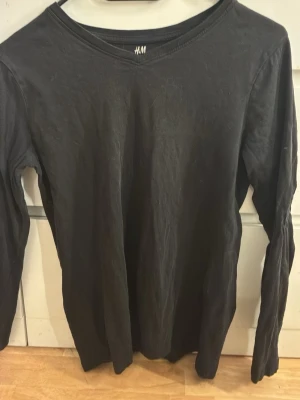 Svart långärmad topp från H&M - En enkel svart långärmad topp från H&M med rund halsringning. Perfekt att styla lager på lager eller bära som den är. Gjord i mjukt material som känns skönt mot huden.