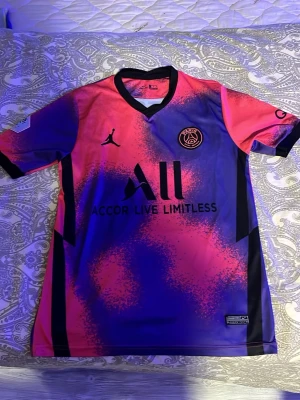 PSG x Jordan matchtröja rosa/lila - Snygg PSG matchtröja i samarbete med Jordan och Nike. Tröjan har en unik rosa och lila färgkombination med svarta detaljer, klubbmärke och sponsortryck på bröstet. Tillverkad i Dri-FIT material som andas, perfekt för fotboll eller träning.