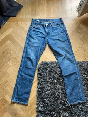Blå raka jeans från Levi's - Klassiska blå jeans från Levi's med rak passform och fem fickor. Jeansen har en ikonisk läderpatch bak i midjan och röda Levi's-detaljer på bakfickan. Tillverkade i slitstark denim med snygga kontrastsömmar. Perfekta för en avslappnad och tidlös stil.