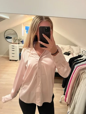 Ljusrosa skjorta med v-ringning - Säljer en ljusrosa skjorta från H&M med v-ringning och klassisk krage. Skjortan har knappar framtill och långa ärmar. 