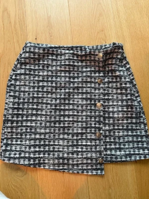 Rutig kortkjol från Vero Moda - Säljer en snygg svartvit rutig kortkjol från Vero Moda. Kjolen har dekorativa knappar framtill och är gjord i ett mjukt material som känns bekvämt. Använd fåtal gånger 