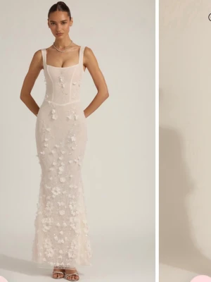 Ljus långklänning med blommor från Oh Polly - Elegant ljus långklänning med smala axelband, snörning i ryggen och 3D-blommor över hela klänningen. Klänningen har figurnära passform och transparenta detaljer som ger en lyxig känsla. Perfekt för speciella tillfällen. Använt klänningen en gång