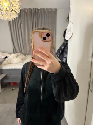 Svart hoodie från Happy Holly - Säljer en svart hoodie från Happy Holly i storlek 40/42. Hoodien har dragkedja framtill med en rund metallring som detalj och är tillverkad i ett mjukt, sammetsliknande material. Perfekt för dig som gillar en avslappnad och stilren look.