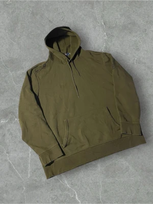 Olivgrön hoodie från Polo Ralph Lauren - Snygg olivgrön hoodie från Polo Ralph Lauren i storlek XXL. Klassisk modell med huva och känguruficka framtill. Tillverkad i mjuk bomullsmix, perfekt för en avslappnad och trendig look. Diskret logga på axeln och ribbade muddar vid ärmslut och nederkant.