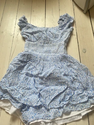 Blommig blå kortklänning Hollister - Söt kortklänning från Hollister i ljusblått och vitt med blommigt mönster. Klänningen har puffärmar, smock i midjan och volangdetaljer. Perfekt för sommarens varma dagar och har en romantisk, feminin stil.