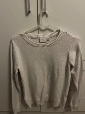 Vit stickad tröja från VILA - Klassisk vit stickad tröja från VILA med rund halsringning och ribbade muddar vid ärmslut och nederkant. Tröjan har en enkel och stilren design, perfekt att matcha med jeans eller kjol. Mjuk och bekväm för kyligare dagar.
