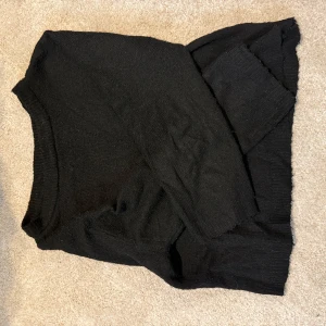 Svart stickad tröja från 157 - En enkel svart stickad tröja från 157 med rund halsringning och långa ärmar. Tröjan har en rak passform och är tillverkad i ett mjukt stickat material som passar perfekt till alla typer av outfits.