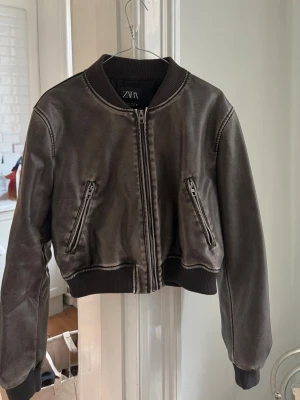 Kort bomberjacka från Zara - Grå/grön bomberjacka från Zara med croppad passform och ribbade muddar vid ärmslut och midja. Jackan har två snedställda dragkedjefickor framtill och stängs med dragkedja. Materialet har en matt finish som ger vintagekänsla. Använd några gånger men fortfarande i fint skick 🖤