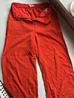 Oranga vida linnebyxor - Snygga röda linnebyxor med avslappnad passform och raka ben. Byxorna har hög midja, dragkedja och knappstängning framtill. Perfekta för en chill och trendig look. Materialet är luftigt linne som känns skönt mot huden.