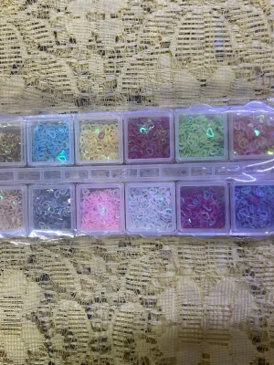 Nageldekorationer i mixade  12 färger - Ett set med nageldekorationer i olika former och färger, inklusive hjärtan, cirklar och andra mönster. Kommer i en praktisk plastask med flera fack. Perfekt för att skapa kreativa och färgglada nageldesigner. Materialet är plast och dekorationerna har glittrig finish. 115kr/låda / bild 