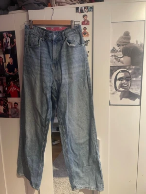 Blå wide leg jeans med hög midja - Säljer ett par ljusblå wide leg jeans med hög midja och klassiska femficksdetaljer. Jeansen har raka ben och är tillverkade i denim. Perfekta för dig som gillar en avslappnad och trendig look. 