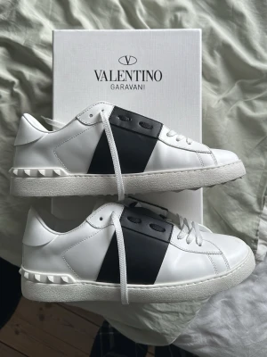Valentino Garavani vita sneakers - Snygga vita sneakers från Valentino Garavani med svart detalj på sidan och klassiska nitar vid hälen. Skorna är helt nya endast använda 1 gång, alla påsar och låda följer med. Pris kan diskuteras vid snabb affär :) Skriv för fler bilder