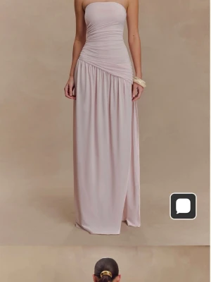 Ljusrosa axelbandslös långklänning - Säljer en elegant ljusrosa långklänning med axelbandslös design och draperad midja. Klänningen har en slits på sidan och är tillverkad i ett mjukt, följsamt material som ger en snygg siluett. Perfekt för dig som vill sticka ut med en stilren look.