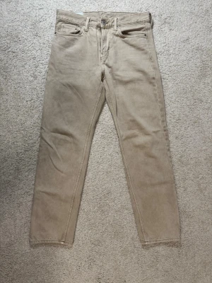 Beige raka jeans från H&M - Säljer ett par beige jeans med rak passform och klassisk design. Jeansen är tillverkade i mjuk bomull och har bälteshällor samt metallnitar vid fickorna. Perfekta för en avslappnad och stilren look. Köptes på H&M 😊